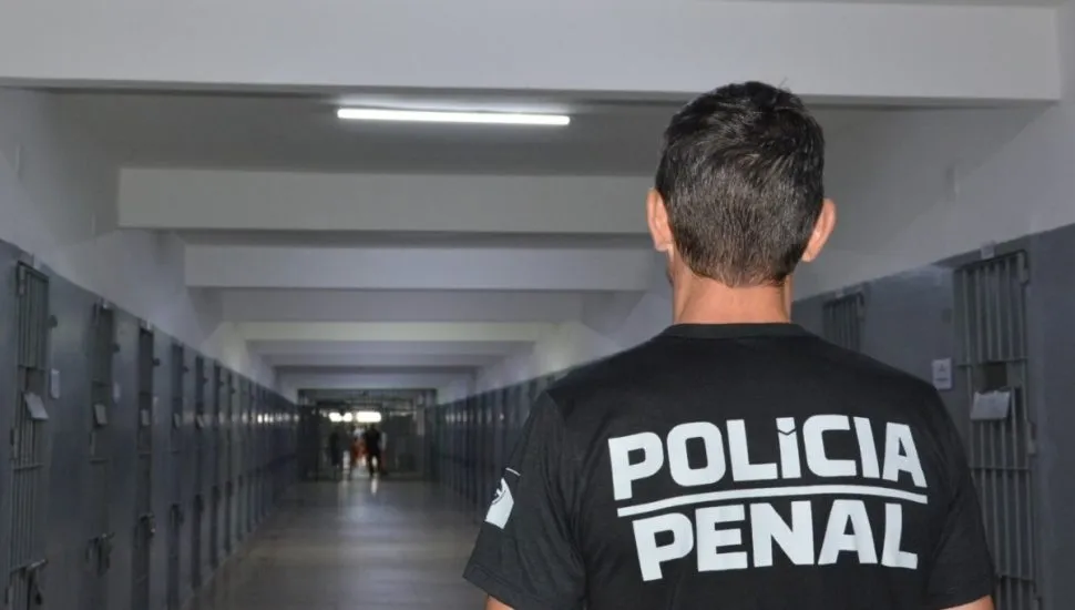 Na imagem, um agente da polícia penal em um corredor entre as celas, dentro de um presídio.