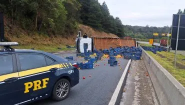 Imagem mostra um caminhão acidentado e uma viatura da PRF na pista.