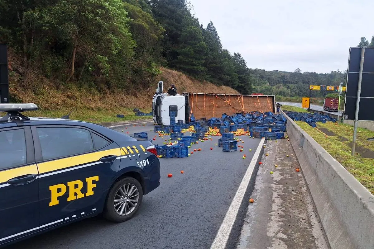 Imagem mostra um caminhão acidentado e uma viatura da PRF na pista.