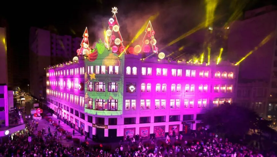 Imagem mostra uma apresentação de Natal no Palácio Avenida, com luzes roxas e milhares de pessoas assistindo.