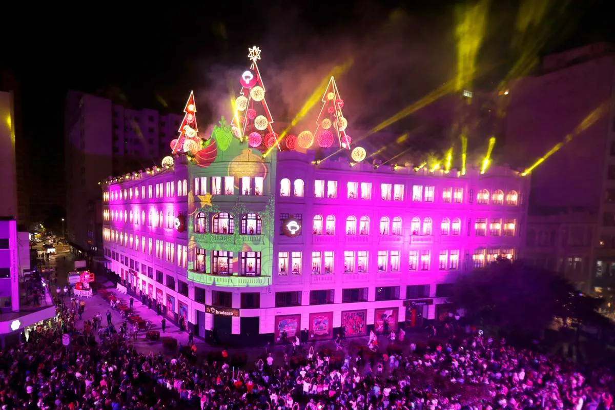 Imagem mostra uma apresentação de Natal no Palácio Avenida, com luzes roxas e milhares de pessoas assistindo.