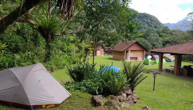 Na imagem, barracas de um acampamento na natureza.