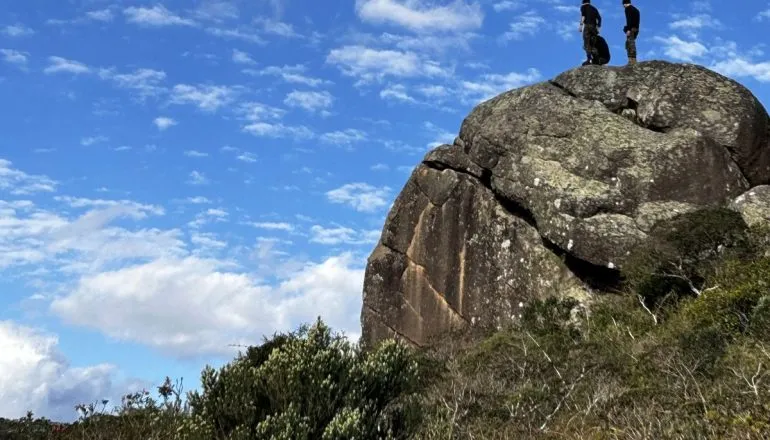 Na imagem, pessoas estão sobre uma pedra, nas montanhas.