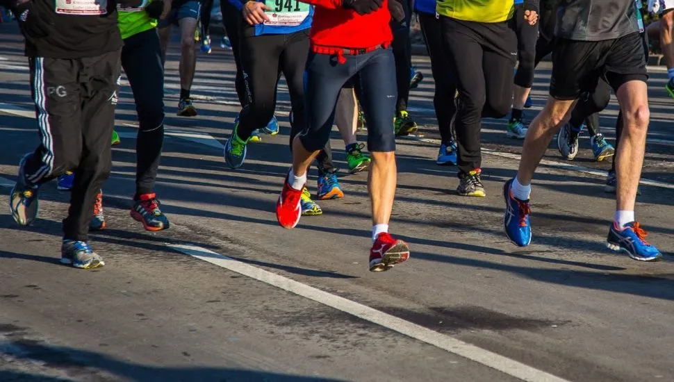 Na imagem, detalhes de atletas, da cintura para baixo, correndo uma prova de corrida de rua.