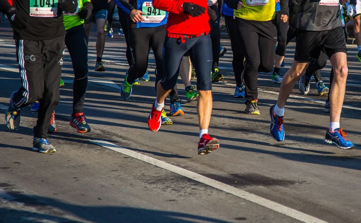 Na imagem, detalhes de atletas, da cintura para baixo, correndo uma prova de corrida de rua.