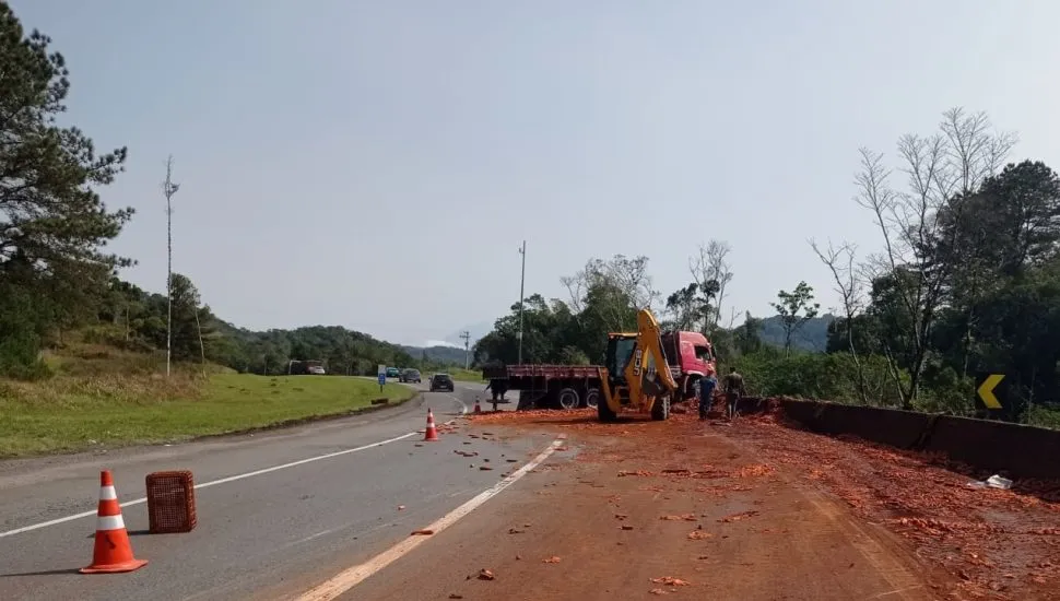 Caminhão atravessado sobre a pista, com carga de cenoura espalhada sobre o asfalto.