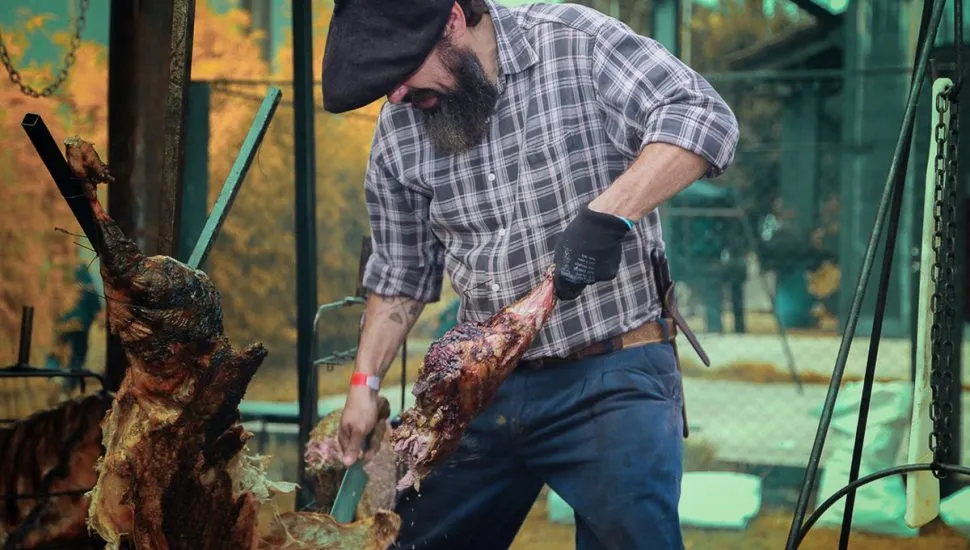 Imagem mostra assados carneando um peril de carneiro no fogo de chão