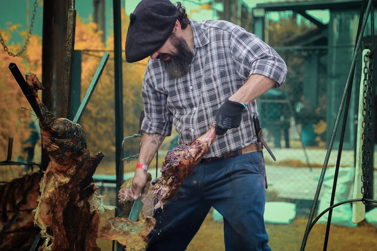 Imagem mostra assados carneando um peril de carneiro no fogo de chão