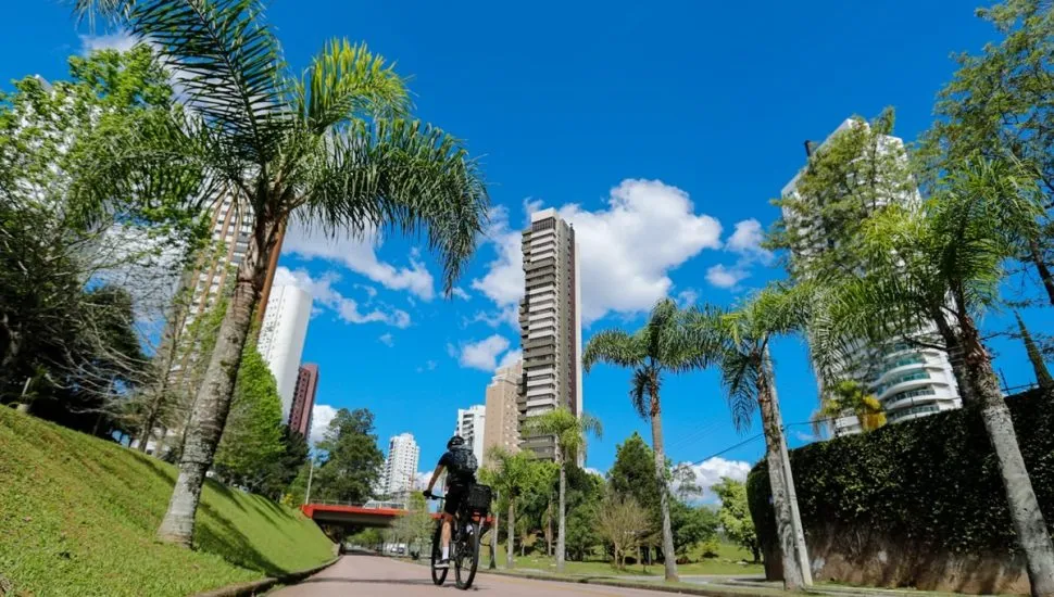 Ciclista pedala pela rua em dia com sol e céu limpo em Curitiba.