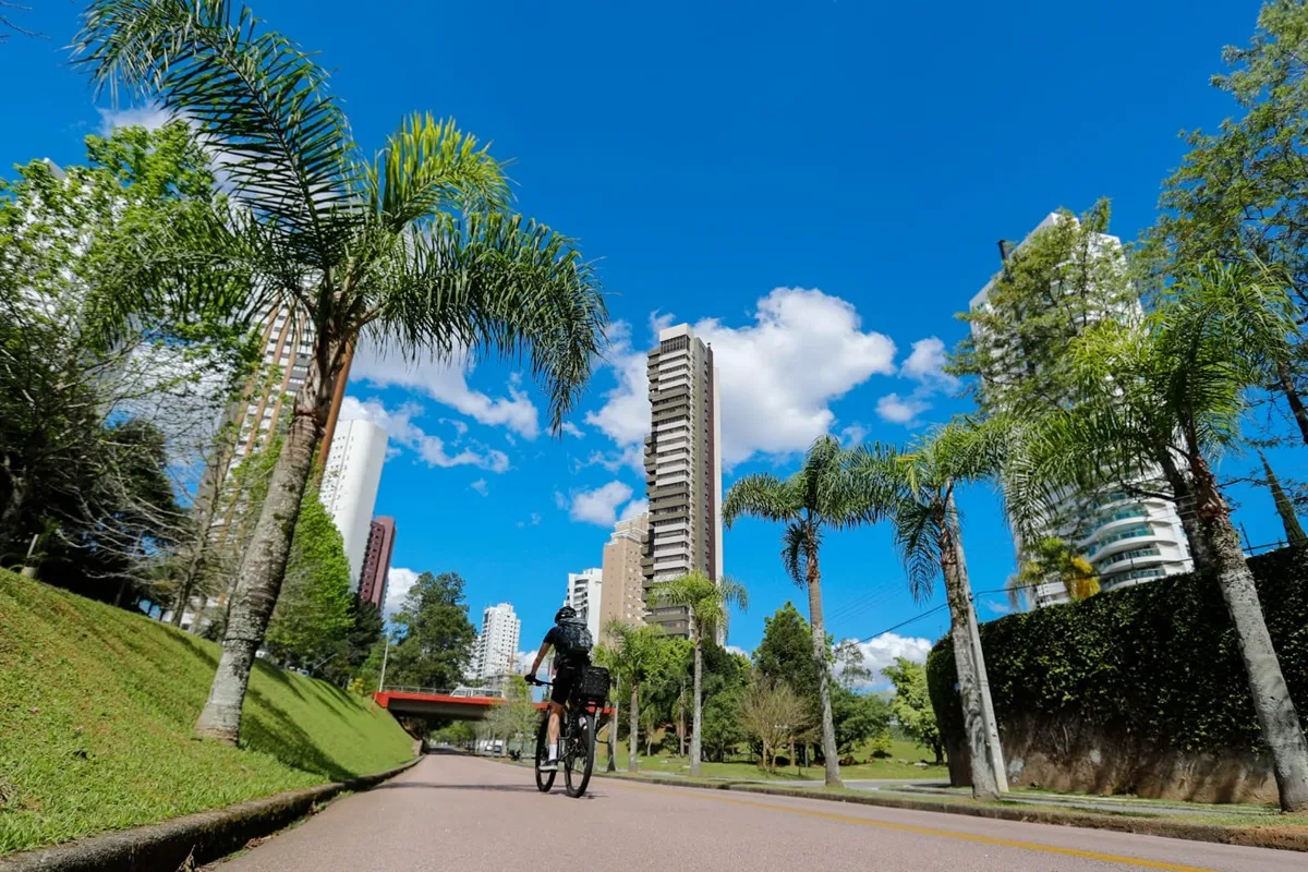 Ciclista pedala pela rua em dia com sol e céu limpo em Curitiba.