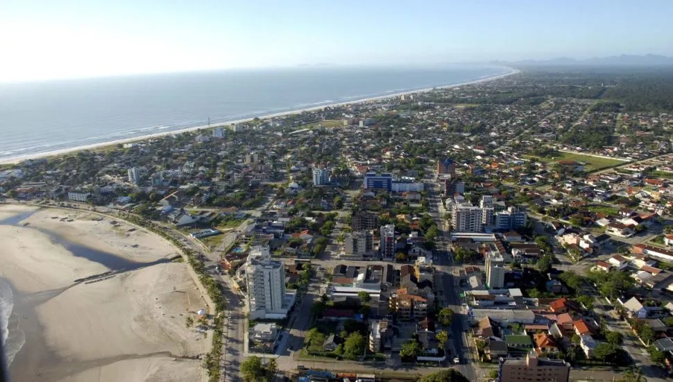 Imagem aérea da cidade de Guaratuba, com mar ao fundo, praia e imóveis.