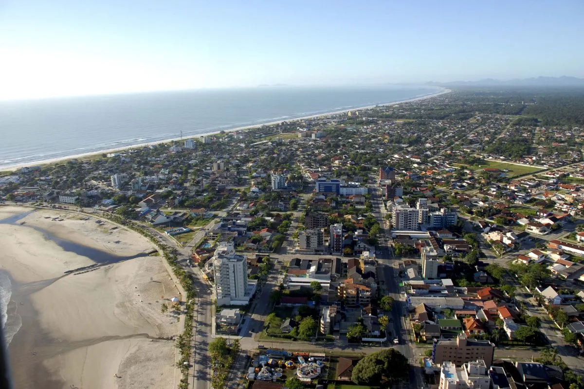 Imagem aérea da cidade de Guaratuba, com mar ao fundo, praia e imóveis.