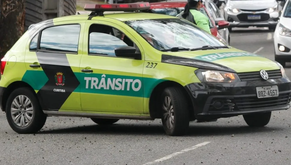 Imagem mostra uma viatura da Setran, parada e bloqueando uma faixa de uma rua. Há uma agente de trânsito atrás do carro, de costas.