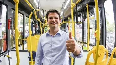 imagem mostra candidato Eduardo Pimentel dentro de um ônibus fazendo sinal de positivo para a câmera