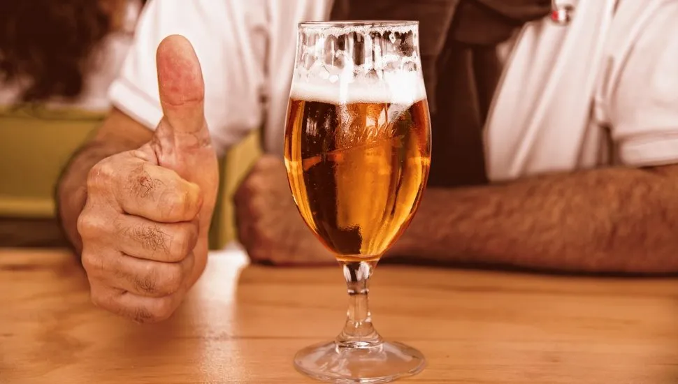 Pessoa com um chope fazendo 'joínha' com a mão.