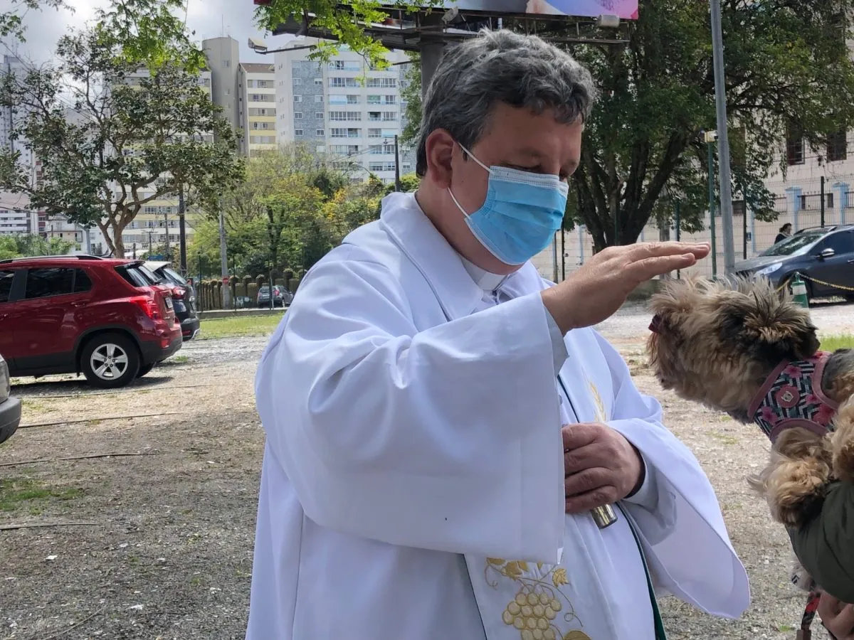 Padre abençoa cachorrinho no colo de tutor.