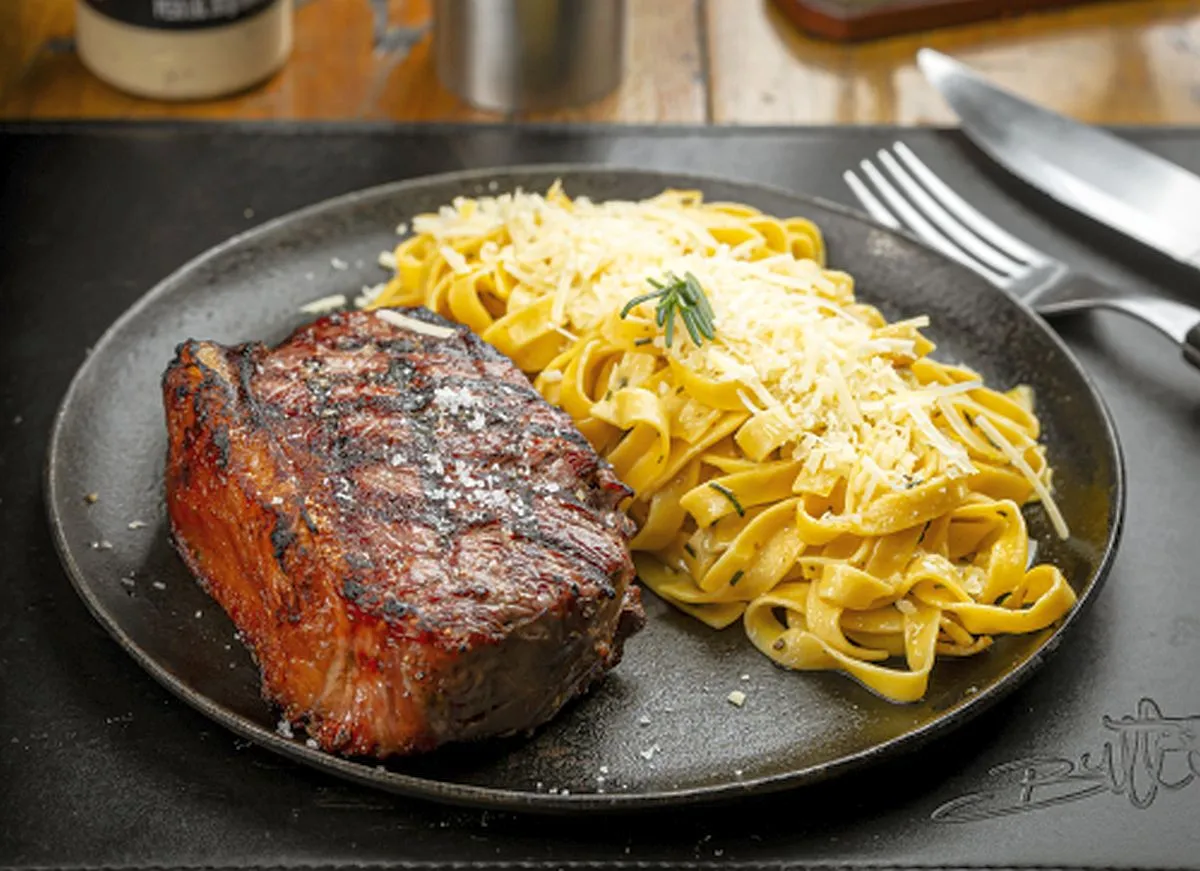 imagem mostra um prato com um steak de contra-filé e uma porção de macarrão com quejo