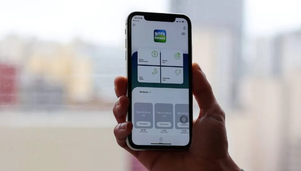 Foto mostra uma pessoa segurando um celular com o aplicativo Nota Paraná aberto.
