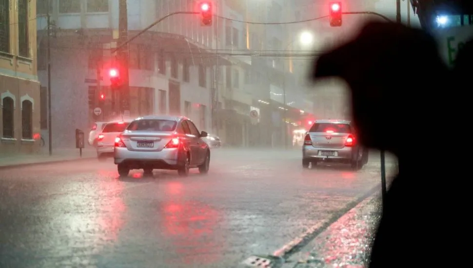 Imagem mostra um carro andando em uma rua de Curitiba com forte chuva e um sinaleiro no vermelho