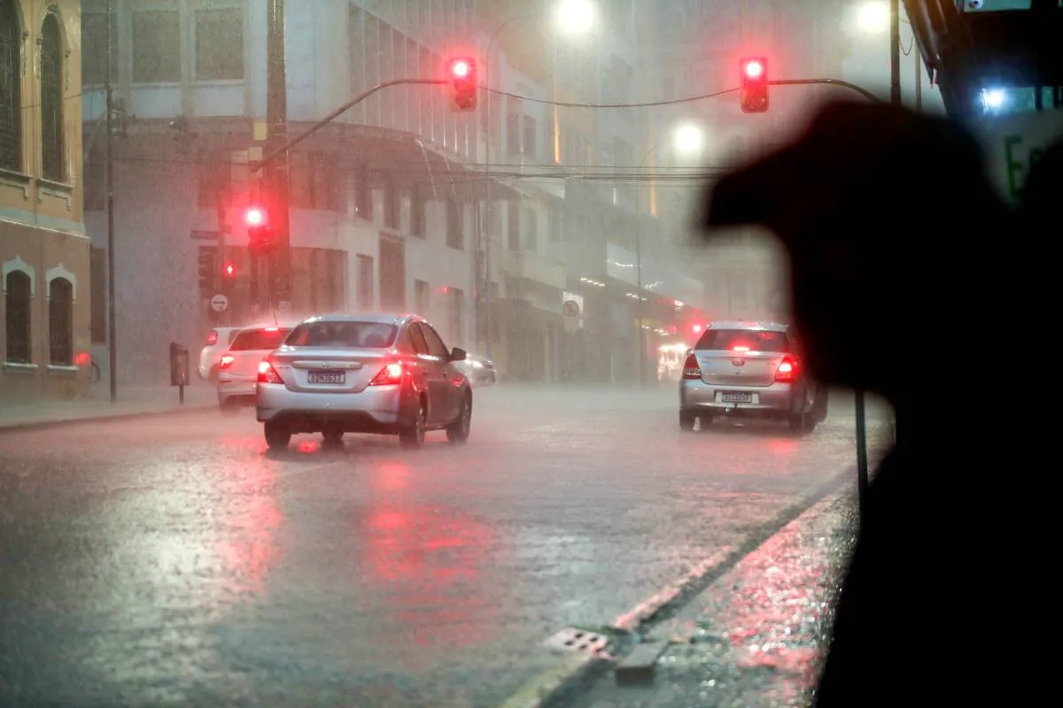 Imagem mostra um carro andando em uma rua de Curitiba com forte chuva e um sinaleiro no vermelho