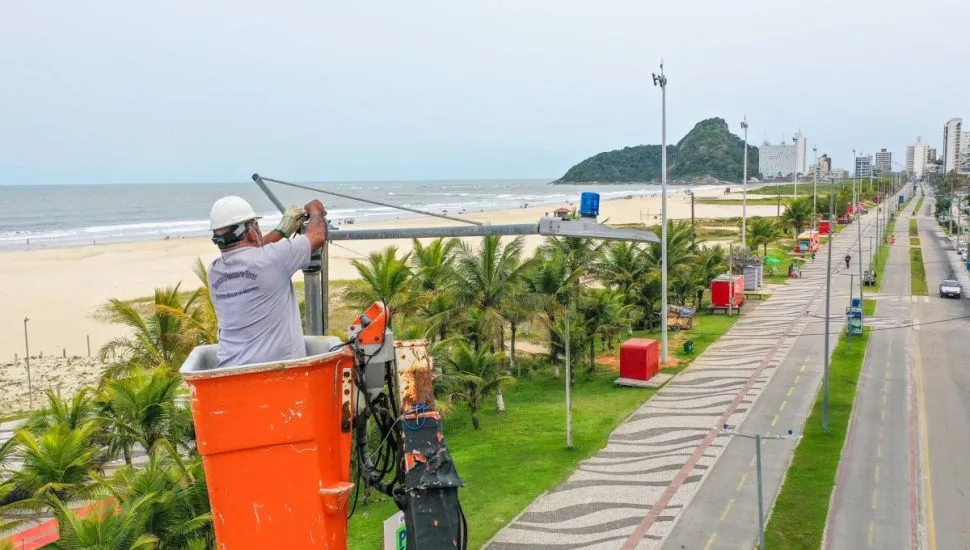 Na imagem, um trabalhador instala um dos novos superpostes. Ao fundo a nova orla de Matinhos.