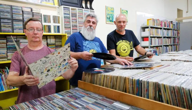 Imagem mostra um trio de amigos entre milhares de discos de vinil.