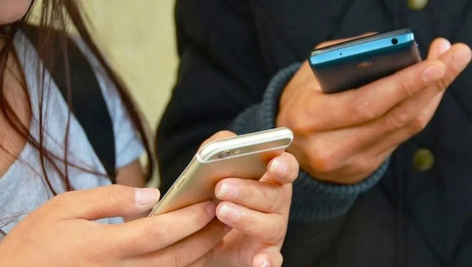 Na imagem, duas pessoas jovens com celulares nas mãos.