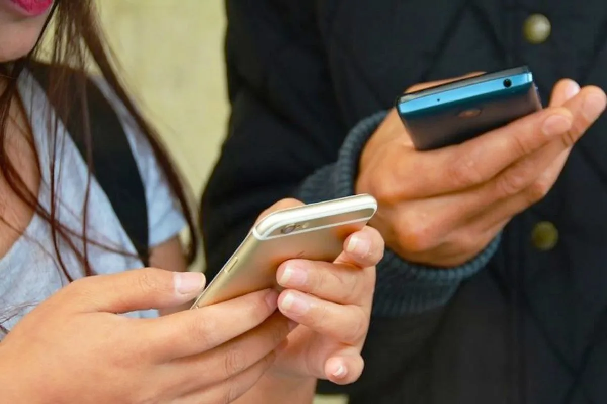 Na imagem, duas pessoas jovens com celulares nas mãos.