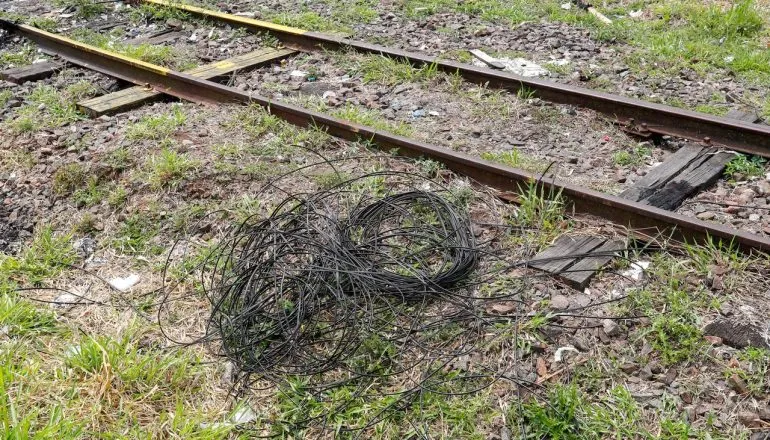 Imagem mostra emaranhado de fios elétricos no chão, ao lado do trilho do trem.