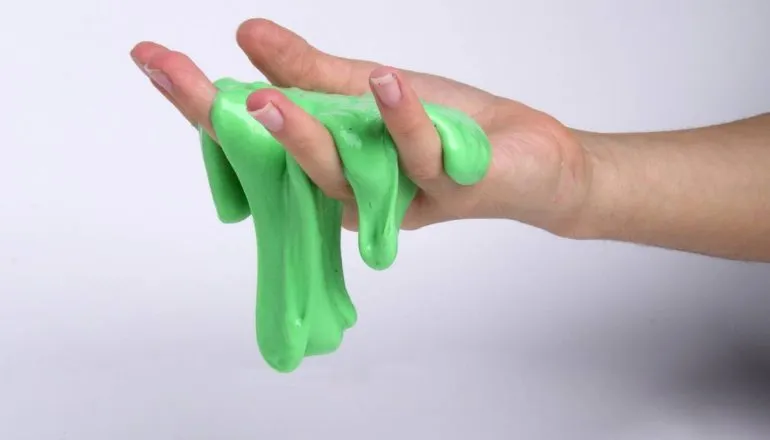 Imagem mostra uma mão segurando um slime verde escorregadio 