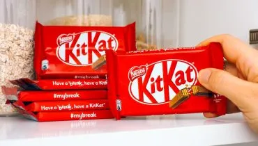 Na imagem, embalagens de barras do chocolate kit kat, empilhadas. Ainda na foto, uma dos chocolates está mão de uma pessoa.