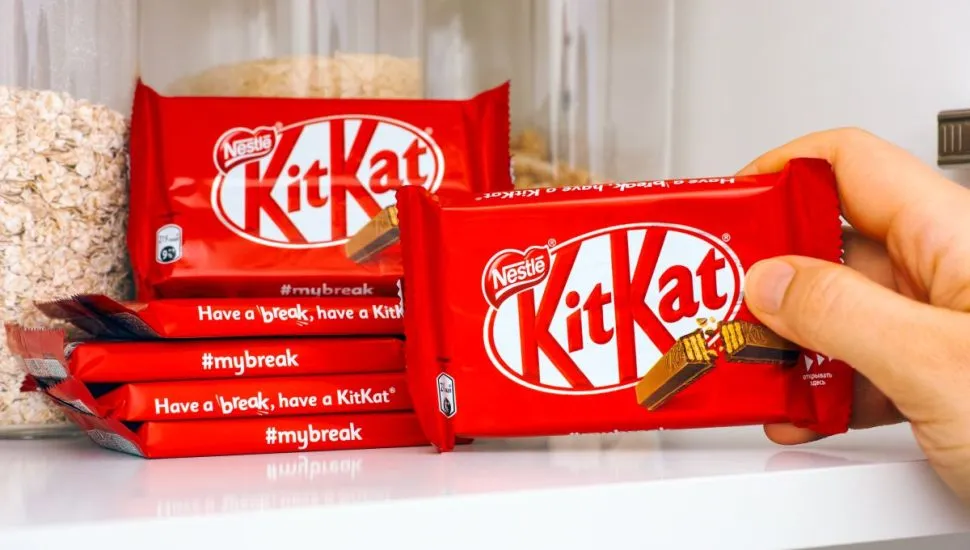 Na imagem, embalagens de barras do chocolate kit kat, empilhadas. Ainda na foto, uma dos chocolates está mão de uma pessoa.