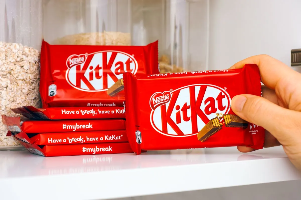 Na imagem, embalagens de barras do chocolate kit kat, empilhadas. Ainda na foto, uma dos chocolates está mão de uma pessoa.