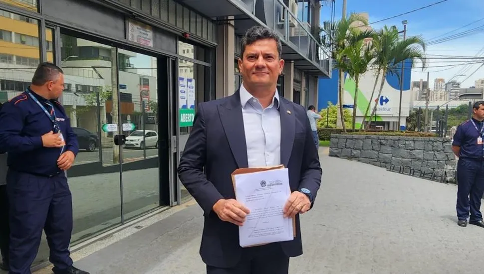 Na imagem, Sergio Moro segura um documento, parado em pé, em frente a um cartório de Curitiba.