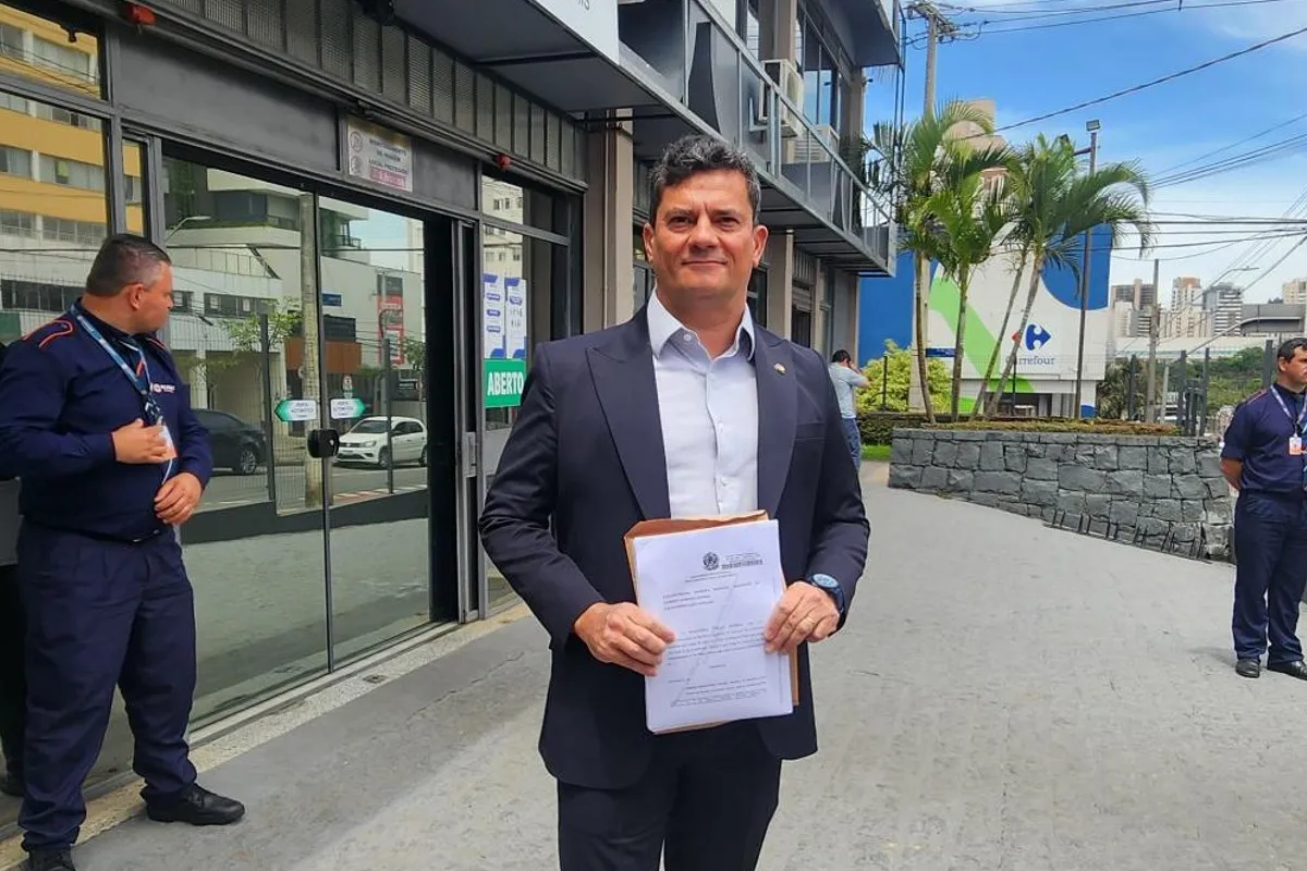 Na imagem, Sergio Moro segura um documento, parado em pé, em frente a um cartório de Curitiba.