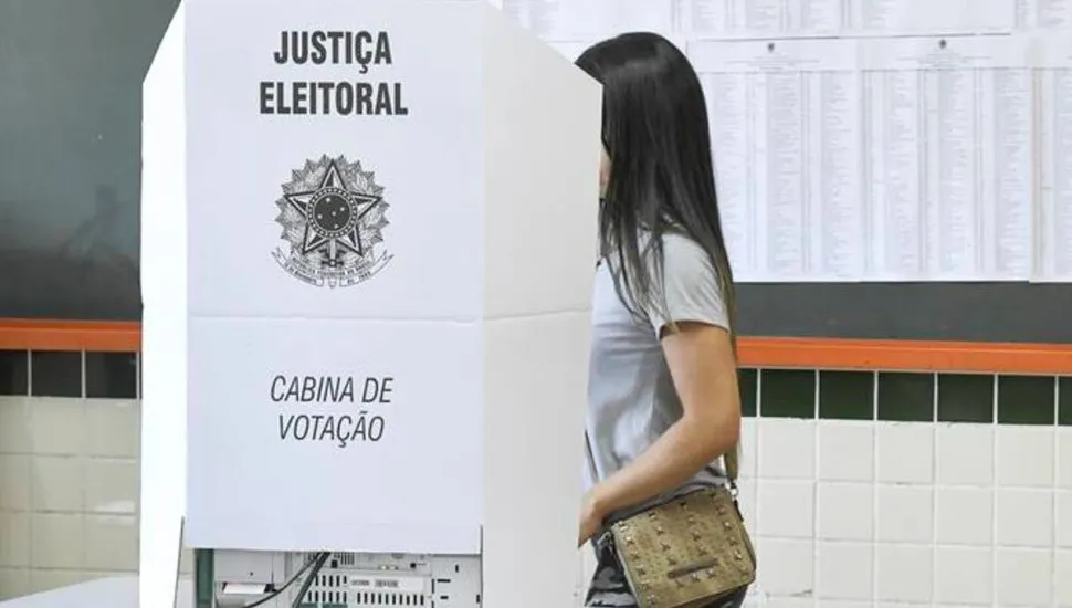 Na imagem, jovem garota vota em uma cabina de votação