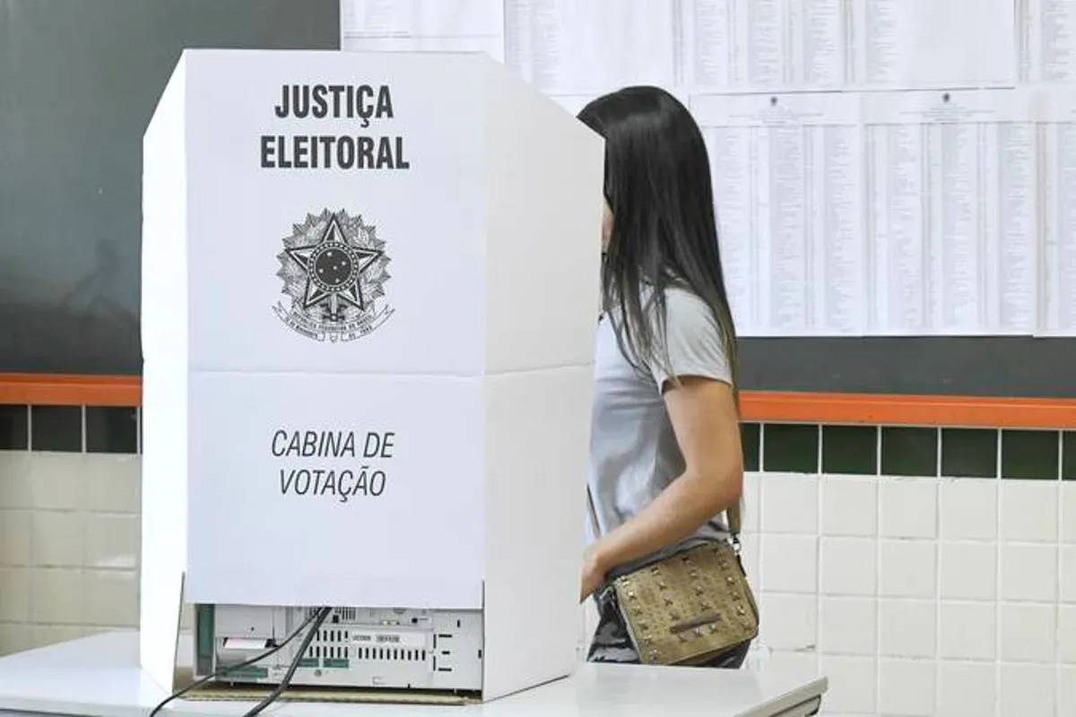 Na imagem, jovem garota vota em uma cabina de votação