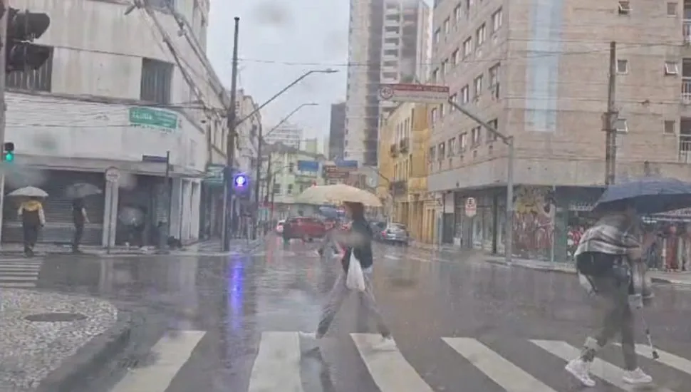 Na imagem, pessoas caminha com guarda-chuvas em rua do Centro de Curitiba.