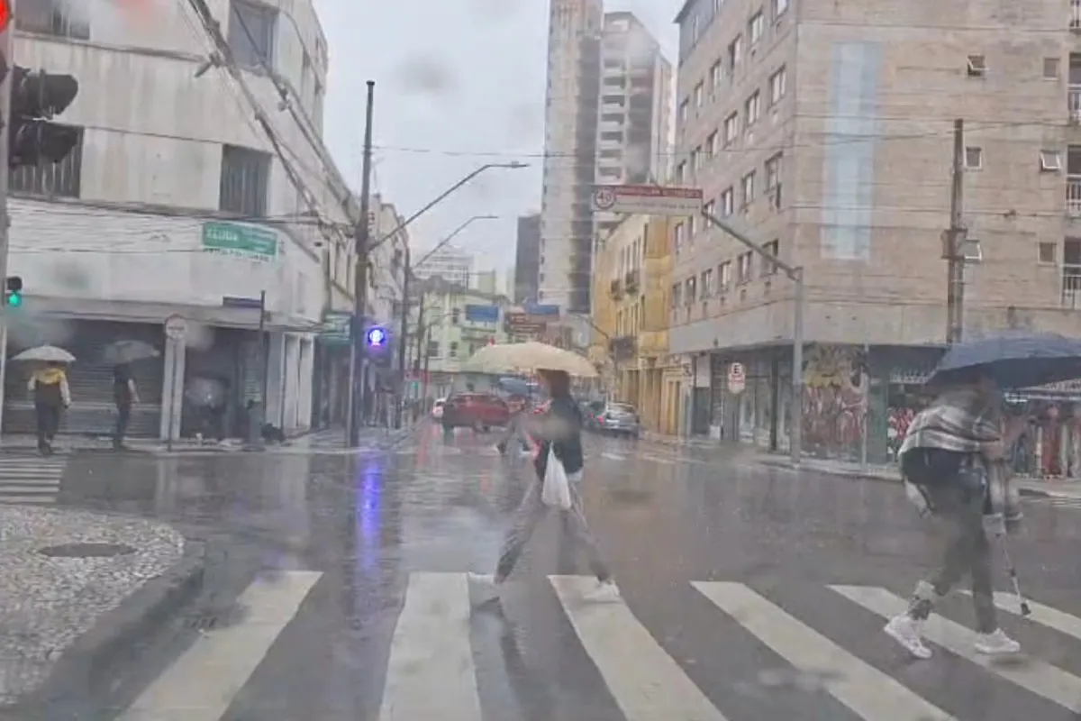 Na imagem, pessoas caminha com guarda-chuvas em rua do Centro de Curitiba.