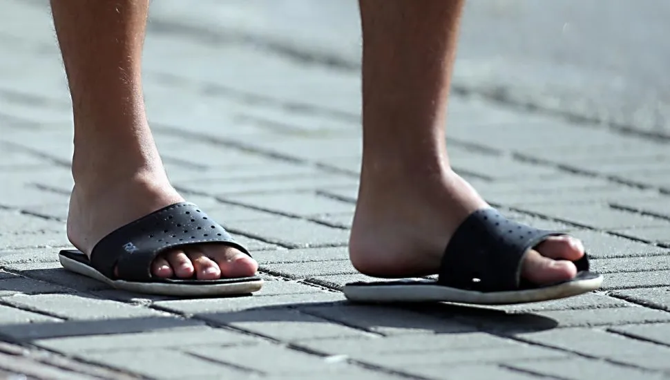 Imagem mostra dois pés masculinos calçando um chinelo em uma calçada de blocos de cimento