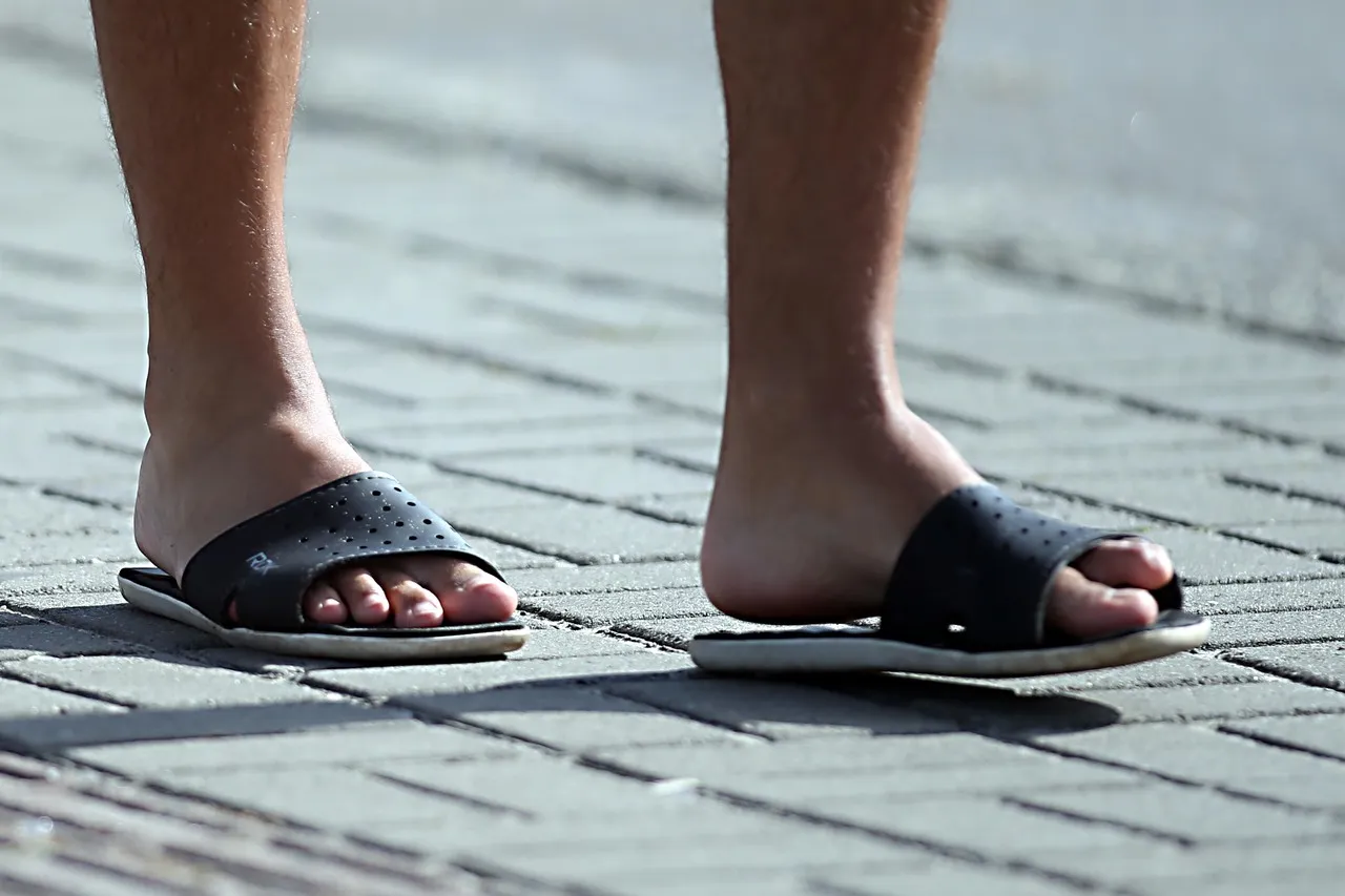 Imagem mostra dois pés masculinos calçando um chinelo em uma calçada de blocos de cimento