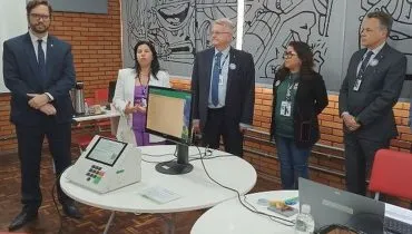 Imagem mostra representantes do TRE em frente a uma mesa com urnas eletrônicas