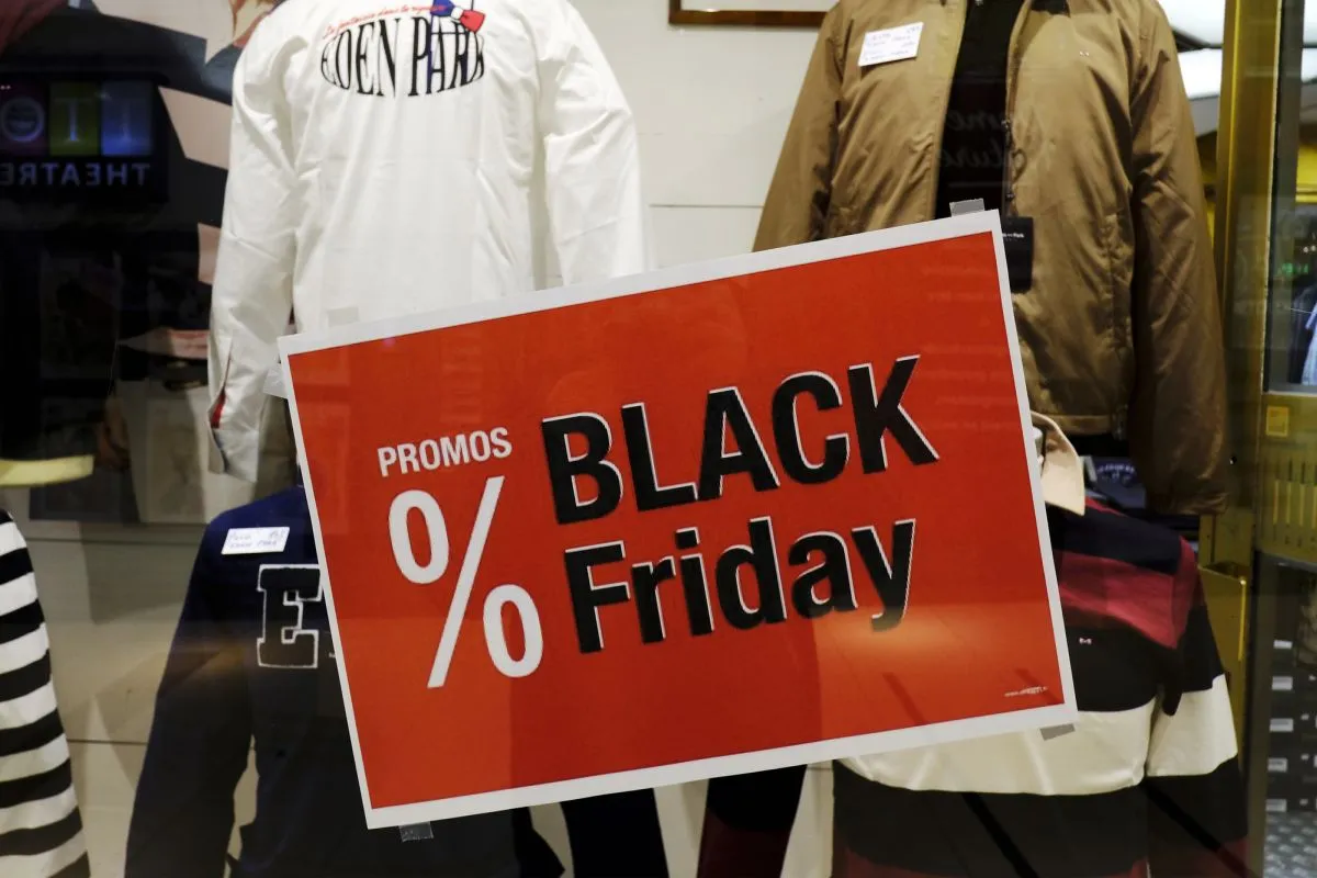 Na imagem, cartaz da black friday na vitrine de uma loja, com roupas atrás.