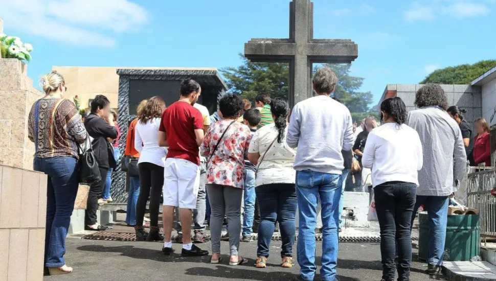 Na imagem, pessoas em volta de uma cruz em cemitério de Curitiba.