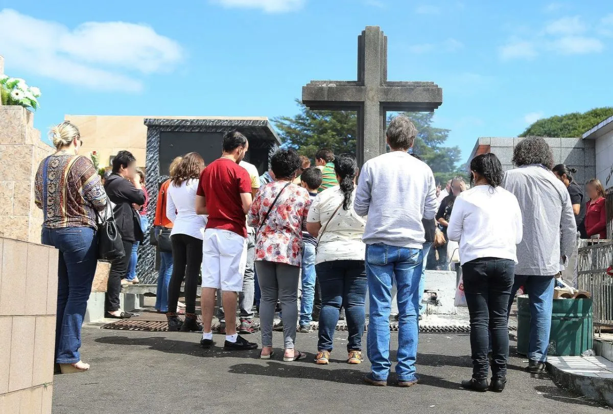 Na imagem, pessoas em volta de uma cruz em cemitério de Curitiba.