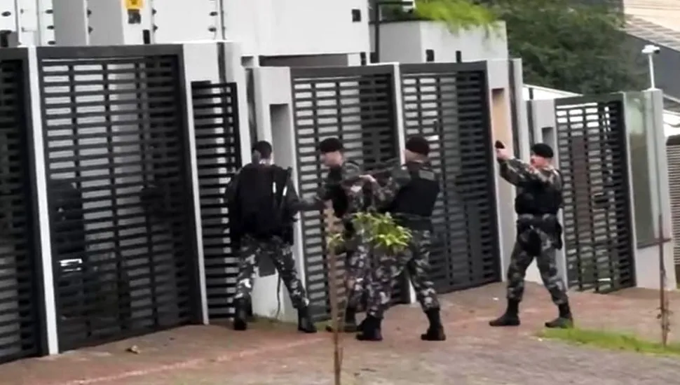 Na imagem, policiais abrem portão de uma residência.