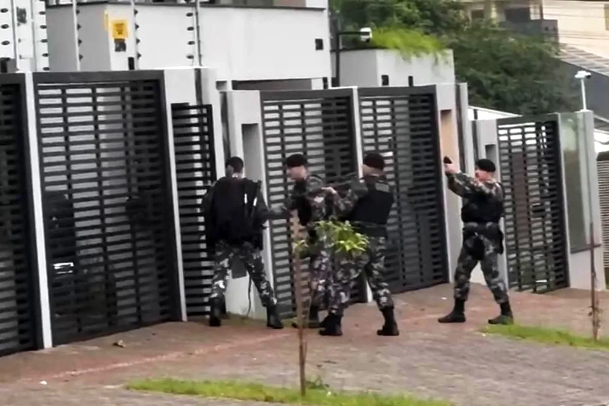 Na imagem, policiais abrem portão de uma residência.