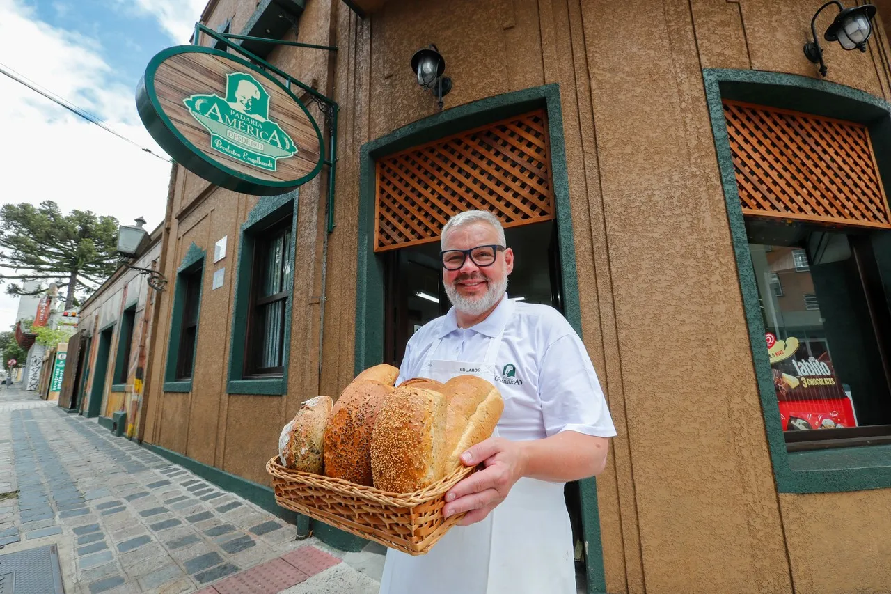 Na imagem, Eduardo Henrique Engelhardt segura cesto com pães na porta da Padaria América, em Curitiba