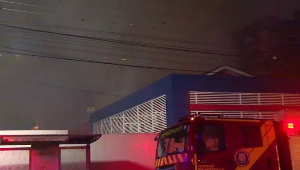 Imagem noturna mostra caminhão dos bombeiros apagando um incêndio em uma escola de inglês de Curitiba.