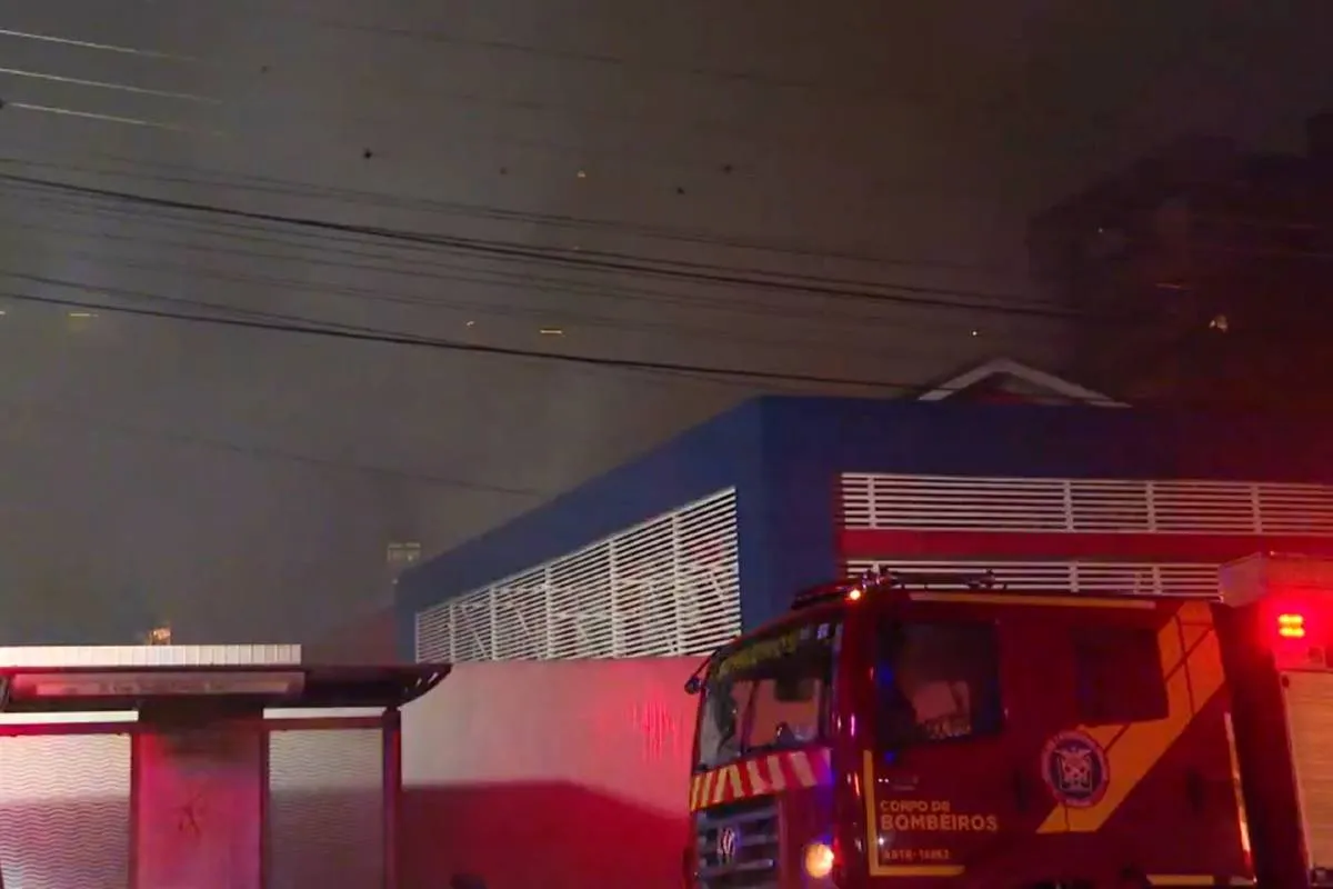 Imagem noturna mostra caminhão dos bombeiros apagando um incêndio em uma escola de inglês de Curitiba.